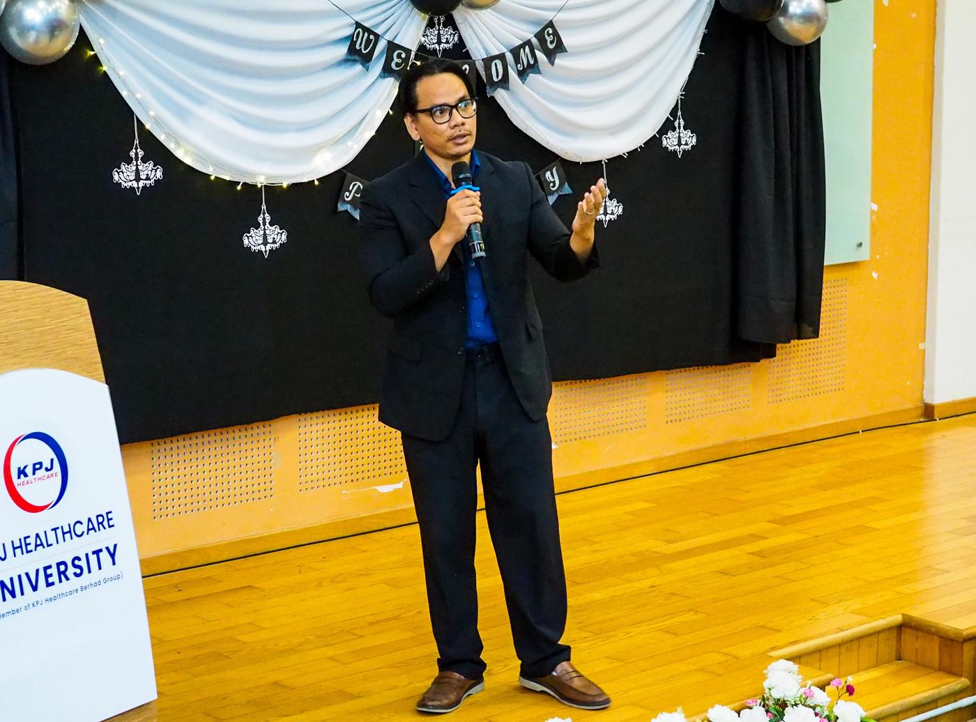 Auf Ali speaking with a microphone on stage at KPJ Healthcare University